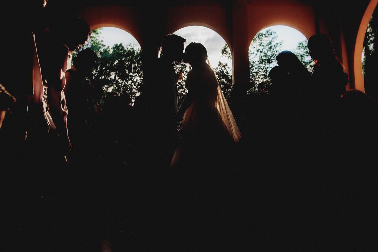 Silhouette of newlyweds kissing in a dramatic wedding ceremony setting.