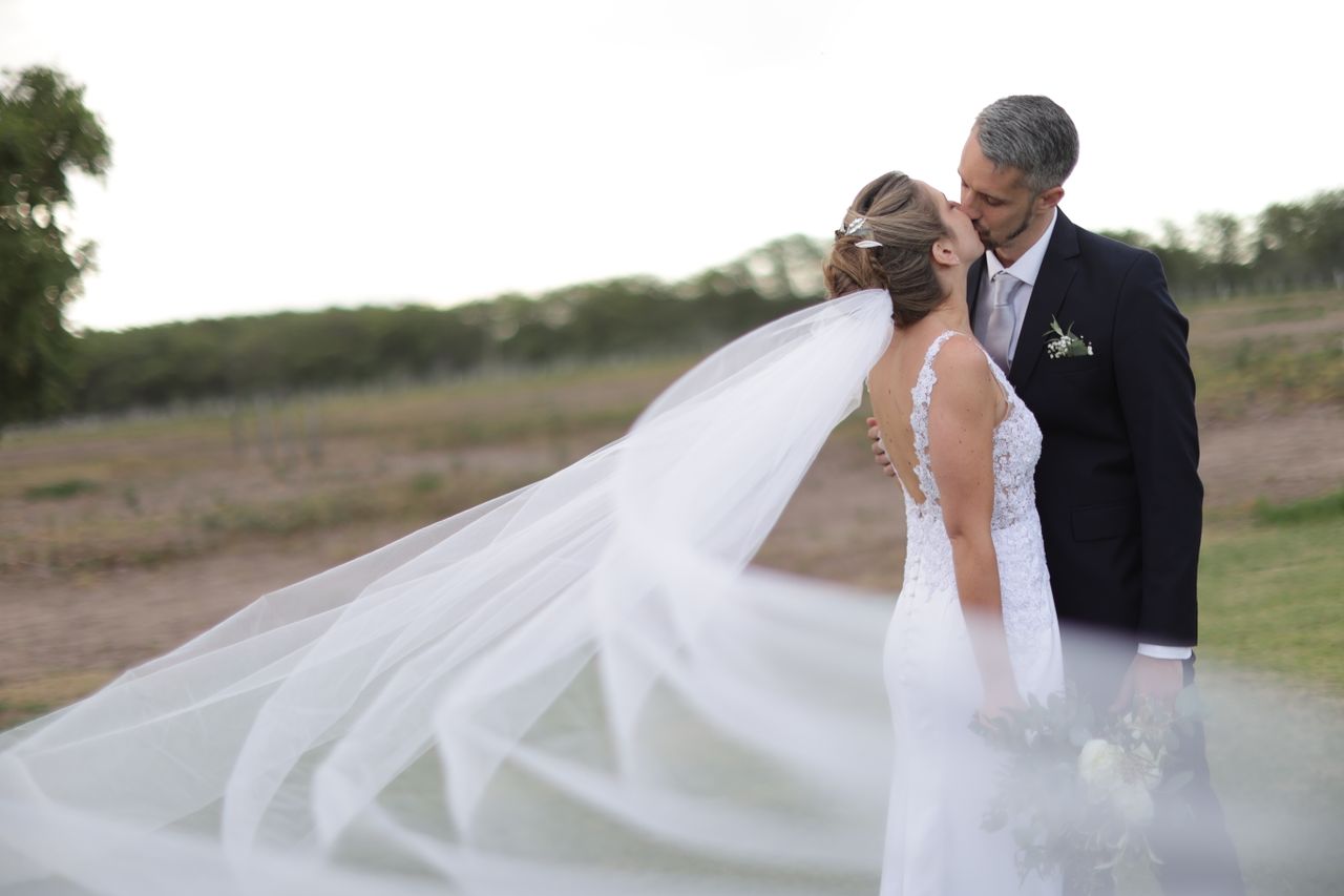 Bride and groom share a tender kiss outdoors with flowing veil.