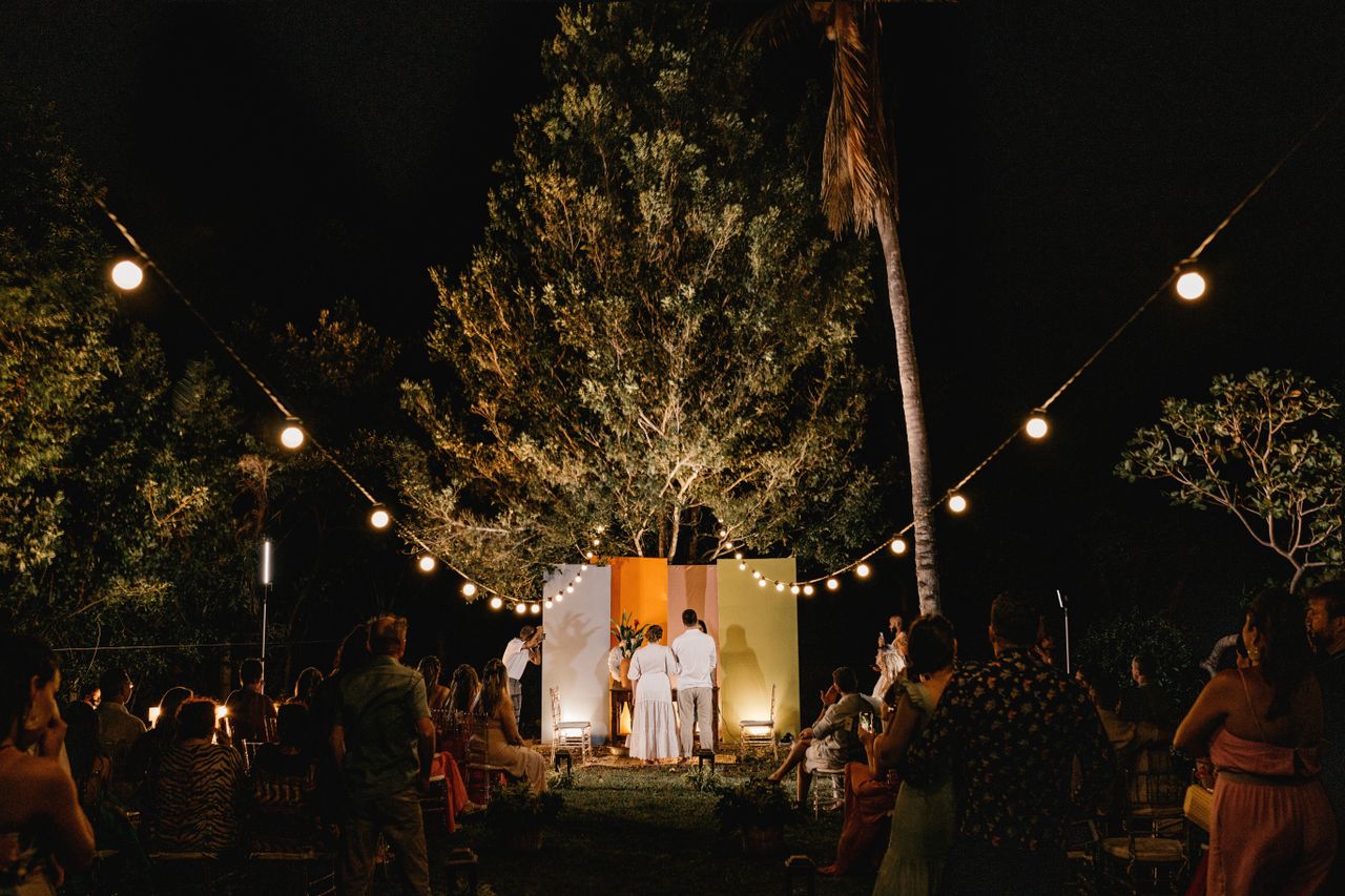 Nighttime outdoor wedding with string lights and guests gathered around.